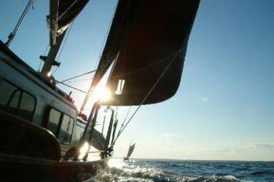 The sun gleams against the Pineapple Ketch as it sails in the open ocean